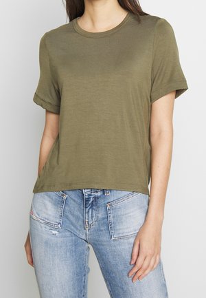 Woman wearing an olive green short-sleeve crew neck t-shirt paired with light blue faded jeans with front pockets.