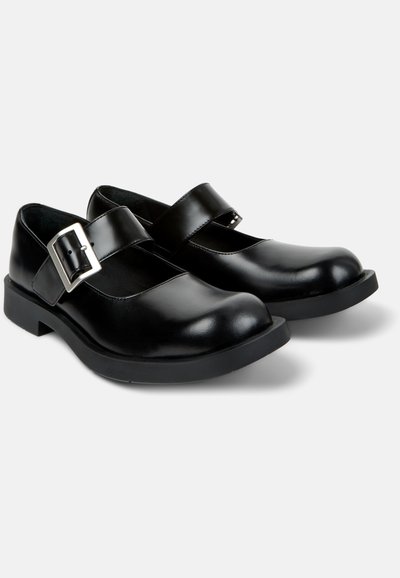 Schwarze Mary-Jane-Schuhe aus Leder mit dicken Gummisohlen und großen silbernen Schnallriemen, nebeneinander auf weißem Hintergrund dargestellt.