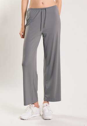 Pantaloni grigi dritti con coulisse, indossati con scarpe da ginnastica bianche su una persona in piedi con le mani rilassate lungo i fianchi.
