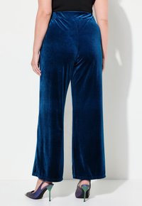 Djupblå sammetsbyxor med vida ben och hög midja. Slät textur, hel längd, matchade med svarta och lila öppen-tå-hälar.