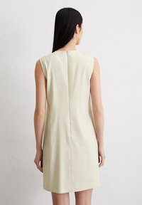 Ärmelloses Kleid aus hellgelbem Stoff mit geradem Schnitt, Rückennahtdetails und einem verdeckten Reißverschluss auf der Rückseite für den Verschluss.
