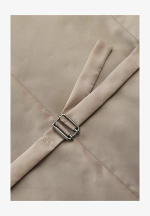 Beige stof med en glat tekstur, der har en metalspænde og en delvist foldet rem. Sømme er synlige.