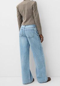 Ljusblå denim vida byxor med hög midja, med bakfickor och subtil blekning. Matching med en strukturerad brun blazer.