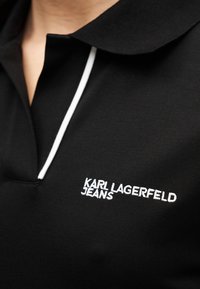 Κοντινή λήψη μαύρου πόλο πουκαμίσου με άσπρη επένδυση και κεντημένο το «KARL LAGERFELD JEANS» στο στήθος.