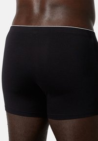 Boxer in cotone nero con design aderente, caratterizzati da un elastico bianco in vita e una texture liscia. Vista posteriore che mostra i dettagli delle cuciture.