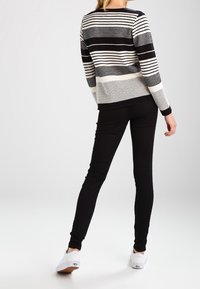Czarny i biały sweter w paski z różnymi wzorami, zestawiony z czarnymi rurkami i białymi sneakersami. Prosty, casualowy design.