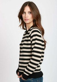 Cardigan a righe in crema e nero, realizzato in morbido tessuto a maglia. Presenta un collo rotondo, bottoni frontali e polsini e orlo a coste.