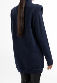 Tmavě modrý vlněný svetr s vysokým límcem, dlouhými rukávy a žebrovanými manžetami a spodním lemem. Texturovaná látka; prodloužená délka vzadu.