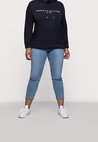 Granatowy hoodie z białym logo i sznurkami, zestawiony z jasnoniebieskimi krótkimi dżinsami i białymi sneakersami. Casualowy zestaw o luźnym kroju.