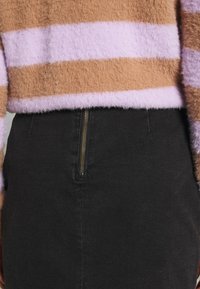 Pruhovaný chlupatý svetr v světle fialové a hnědé, spárovaný s černou sukní s viditelným zlatým zipem a texturovanou látkou.