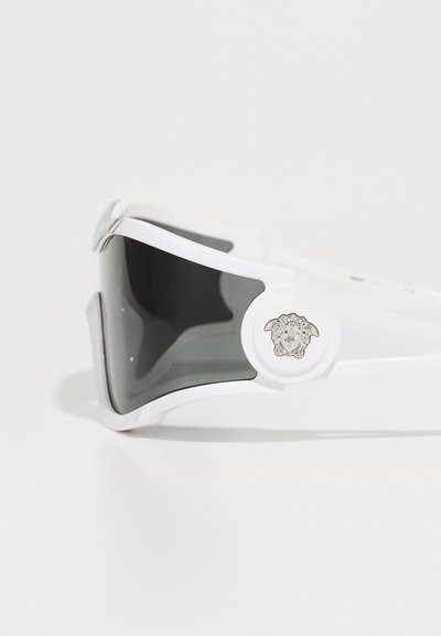 White sports sunglasses with a sleek design, gray lenses, and a decorative silver emblem on the frame.