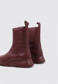 Botas tobilleras de cuero burdeos con un acabado texturizado, suela de goma, doble tirador y marca en el lateral. Diseño de suela gruesa.