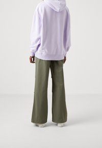 Sweatshirt con cappuccio di un leggero color viola con una vestibilità comoda, abbinato a pantaloni larghi di un verde oliva realizzati in un tessuto morbido, e scarpe bianche.