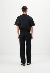 Zwarte shirt met korte mouwen en witte stiksels, gecombineerd met zwarte broek met een elastische tailleband en een enkele achterzak.