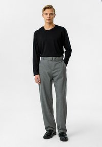 Zwarte lange mouwen shirt, grijze high-waisted broek met een riem. Glad stof met subtiele textuur en een getailleerde pasvorm, gecombineerd met zwarte schoenen.