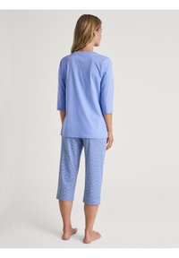 Lichtblauw shirt met driekwart mouwen en bijpassende geknipte pyjama-onderdelen met een hartjespatroon. Zacht, lichtgewicht stof.