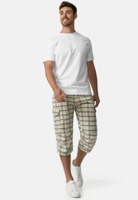 T-shirt blanc à col rond associé à un short cargo à carreaux beige avec une coupe mi-genoux et des poches, complété par des baskets blanches.