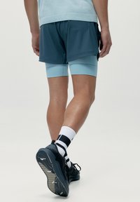 Idrottsshorts i mörkblått med ljusblå kompressionsunderbyxor, tillsammans med svarta sneakers och svart-vitt randiga strumpor.