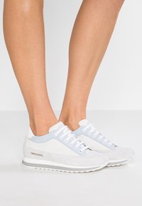 Vita och ljusblå sneakers med mocka vid tån och på sidorna, med vita snören och en grå gummisula. Logotyp på utsidan.