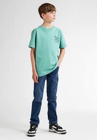 Tricou din bumbac verde mentă cu un grafic frontal, asortat cu blugi albaștri și adidași negri și albi. Design simplu și croială confortabilă.