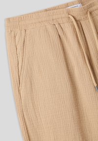 Joggers beige e texturizzati con cintura elasticizzata a costine e cordino. Due tasche laterali, tessuto leggero e vestibilità rilassata.