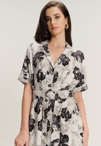 Kwiatowa sukienka na guziki w czarno-białym kolorze, z krótkimi rękawami, dopasowaną talią z paskiem oraz teksturowanym materiałem.