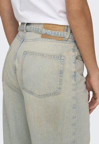 Jeans de mezclilla azul claro con cintura alta, que presentan una etiqueta de cuero con el nombre de la marca y dos bolsillos traseros con detalles de costura.