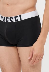 Boxer shorts neri in cotone con un elastico bianco in vita che presenta il nome del marchio "DIESEL" in grassetto nero. Texture liscia e design aderente.