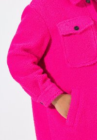 Chaqueta de forro polar en un brillante color rosa con un acabado texturizado. Cuenta con un bolsillo en el pecho, cierre de botones y bolsillos laterales en un diseño de ajuste relajado.