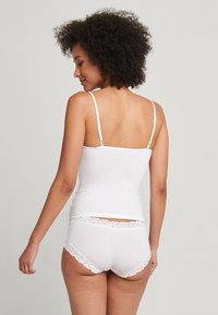 Top senza maniche bianco con spalline sottili, abbinato a mutandine bianche con bordo in pizzo. Design semplice, texture liscia. Vista posteriore.