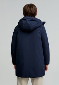 Marineblå isoleret jakke med hætte, med en lige pasform, glat tekstur og sømdetaljer langs siderne og ryggen.