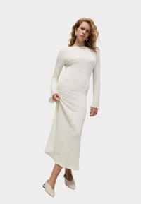 Abito bianco a maniche lunghe con tessuto testurizzato, design aderente e spacco laterale. Presenta un collo rotondo e accenti di polsino arricciato.