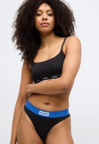 Must rinnahoidja logoga paelaga ja sobivad mustad stringid sinise elastse vööga, mille ees on logomärgiga silt.