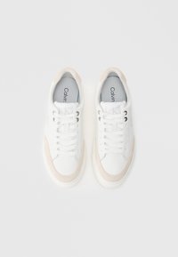 Λευκά αθλητικά παπούτσια με μπεζ σουέντ λεπτομέρειες, διαθέτουν στρογγυλή μύτη, επίπεδα κορδόνια και ασημένιες οπές. Λογότυπο "Calvin Klein" στη γλώσσα.