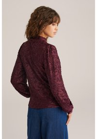 Bordinės spalvos siuvinėta palaidinė ilgomis rankovėmis, su gėlių raštu ir aukštu apykakle. Derinama su mėlynais džinsiniais kelnėmis.