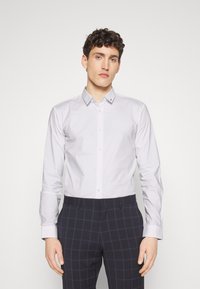 Light gray long-sleeve shirt with a pointed collar, buttoned front, and structured fit. Paired with navy plaid trousers.