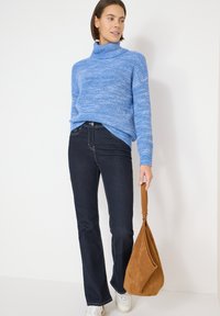 Pull à col roulé en maille bleu clair associé à un jean évasé bleu foncé. Un sac à bandoulière en suède marron complète la tenue, avec des baskets blanches.