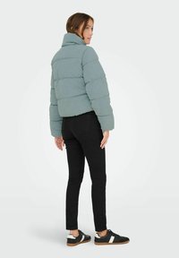 Lichtblauwe gewatteerde jas met een hoge kraag, doorgestikt ontwerp en brede mouwen. Gecombineerd met zwarte skinny jeans en zwarte sneakers.