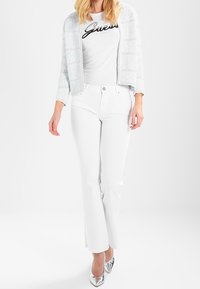 Vita utsvängda jeans som kombineras med en vit t-shirt med grafik och svart text, samt en ljusblå strukturerad kort cardigan. Silverfärgad hög klack.