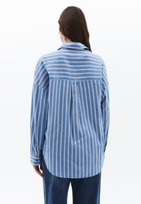 Camicia a righe blu realizzata in tessuto leggero, con maniche lunghe, colletto e vestibilità ampia, caratterizzata da righe verticali e orizzontali.