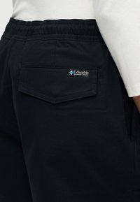 Gros plan sur un pantalon à taille élastique noire avec une poche à rabat au dos et le logo Columbia Sportswear sur la poche.