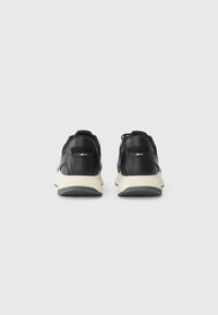 Black sneakers with a textured leather upper, padded collar, and contrasting cream rubber sole. Features ventilation accents on heel.