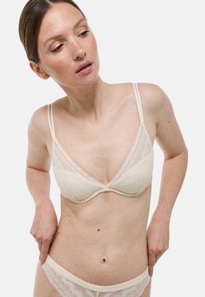 Bralette crème avec des dentelles, de forme triangulaire, doté de fines bretelles ajustables et de motifs géométriques délicats sur le tissu.