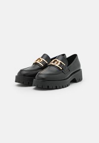 Black leather loafers with a chunky platform sole, featuring a gold hardware accent on the front. Smooth texture and sleek design.