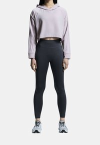 Kratká mikina světle růžové barvy, s kapucí a raglánovými rukávy, kombinovaná s černými legínami s vysokým pasem a bílými sportovními botami.