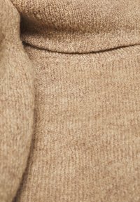 Beige gebreide stof met een gestructureerd oppervlak, met een zachte, vuzzy uitstraling en subtiele variaties in kleur en patroon.