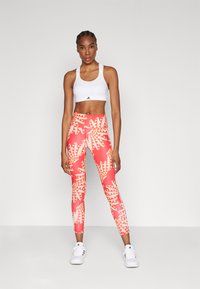 Top desportivo branco e leggings vermelhas com padrão geométrico de folhas amarelas. As leggings têm uma cintura alta e uma textura lisa e elástica.