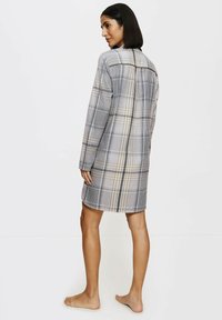 Kárované šaty v béžové, modré a černé barvě. Dlouhé rukávy, límeček a délka po střední stehna s volným střihem a minimálními detaily.