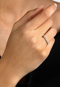 Silberner Ring mit einem dünnen Band, verziert mit kleinen, klaren Steinen, getragen an einer Hand mit hellem Hautton. Einfaches, elegantes Design.