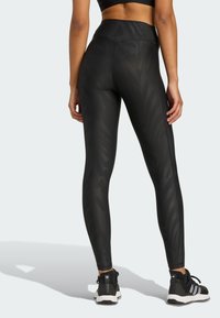 Hoch geschnittene schwarze Leggings mit einem dezenten Zebra-Muster, aus dehnbarem Material gefertigt. Kombiniert mit schwarzen Sportschuhen mit weißen Akzenten.